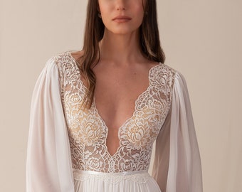 Könnte beinhalten: Ein weißes Brautkleid mit tiefem V-Ausschnitt und langen Ärmeln. Das Kleid ist aus einem durchsichtigen Stoff mit Spitzendetails gefertigt. Die Ärmel sind bauschig und haben Spitzenmanschetten. Das Kleid hat ein figurbetontes Oberteil und einen fließenden Rock.