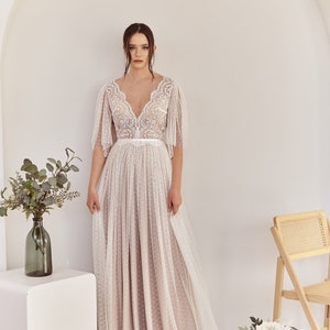 An ivory lace wedding dress with a v-neckline and a fitted bodice. The skirt is made of a sheer fabric with polka dots and has a flowing silhouette. The dress has a belt at the waist and short sleeves. Lace & Love Bohemian Wedding Dresses.