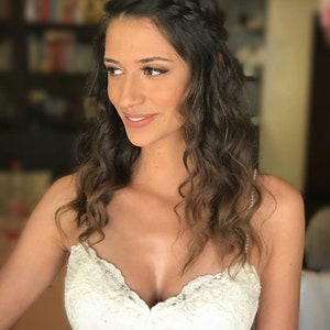 May include: A bride with long, wavy brown hair styled in a braid. She is wearing a white lace wedding dress with a sweetheart neckline.