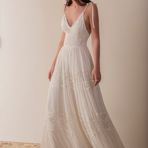 May include: A white sleeveless maxi dress with a lace bodice and a flowing skirt. The dress has a V-neckline and thin straps that tie at the shoulders.