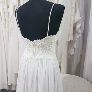 May include: A white wedding dress with a lace bodice and a flowing skirt. The dress is on a mannequin and is displayed in a bridal shop.