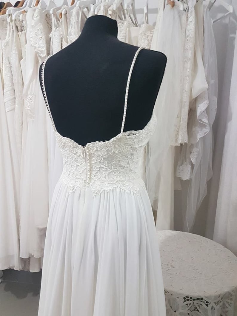 May include: A white wedding dress with a lace bodice and a flowing skirt. The dress is on a mannequin and is displayed in a bridal shop.
