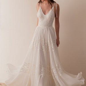 Puede incluir: Un vestido de novia blanco de encaje con una falda fluida y tirantes finos. El vestido tiene un corpi&ntilde;o ajustado y un escote en V.