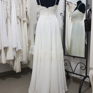 May include: A white wedding dress with a lace bodice and a flowing skirt. The dress has a sweetheart neckline and thin straps. The skirt is made of a soft, flowing fabric and has a lace trim at the hem.