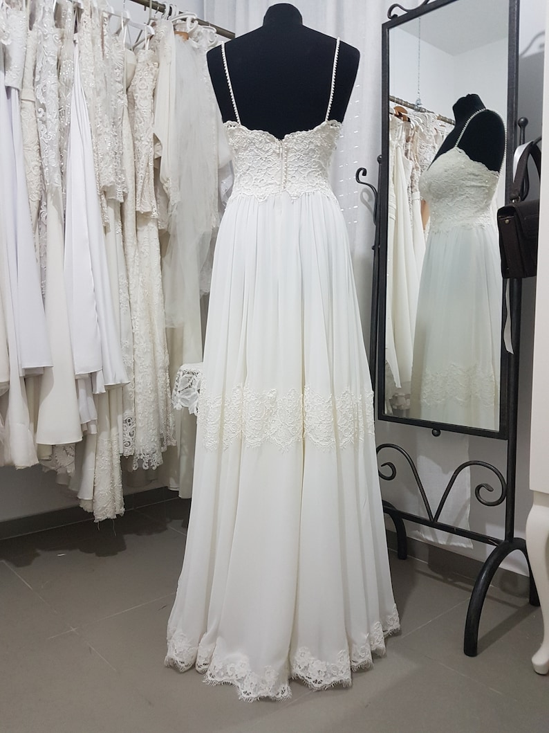 May include: A white wedding dress with a lace bodice and a flowing skirt. The dress has a sweetheart neckline and thin straps. The skirt is made of a soft, flowing fabric and has a lace trim at the hem.