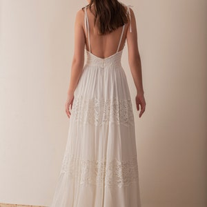 May include: A white sleeveless maxi dress with a lace overlay and a low back. The dress has a flowing skirt and a fitted bodice.