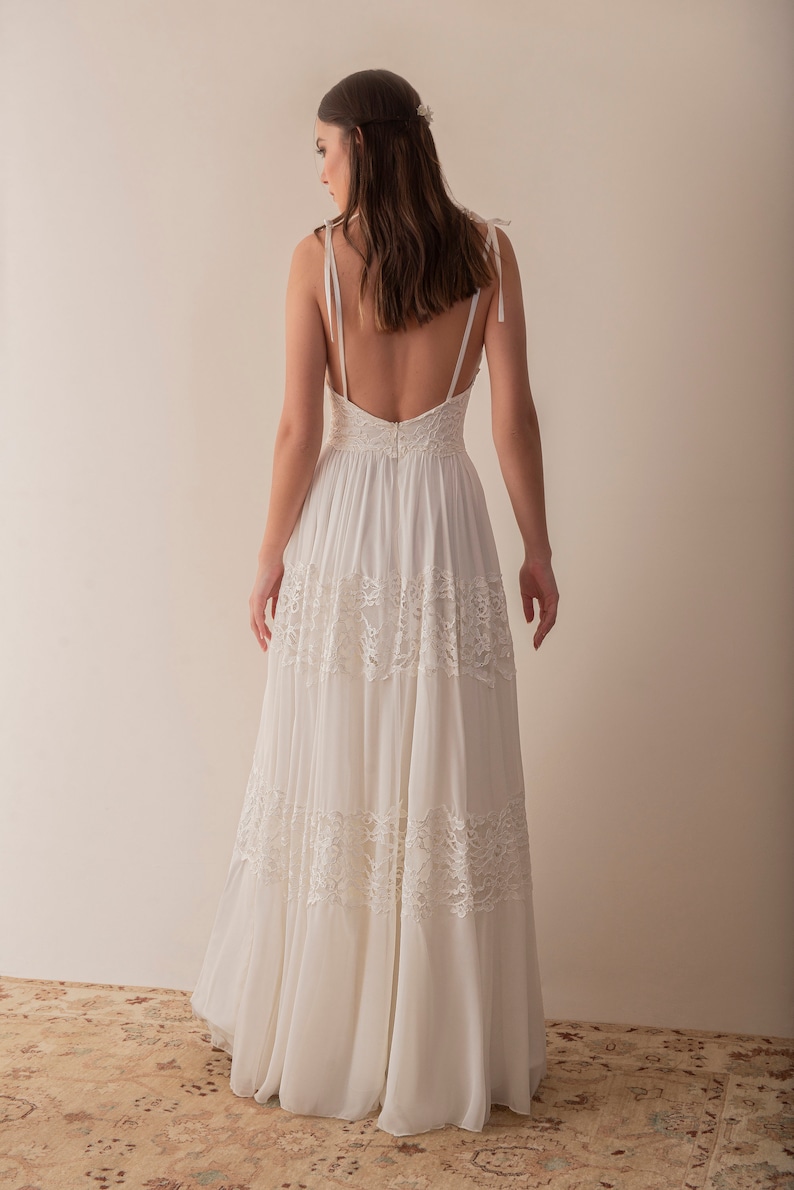 May include: A white sleeveless maxi dress with a lace overlay and a low back. The dress has a flowing skirt and a fitted bodice.