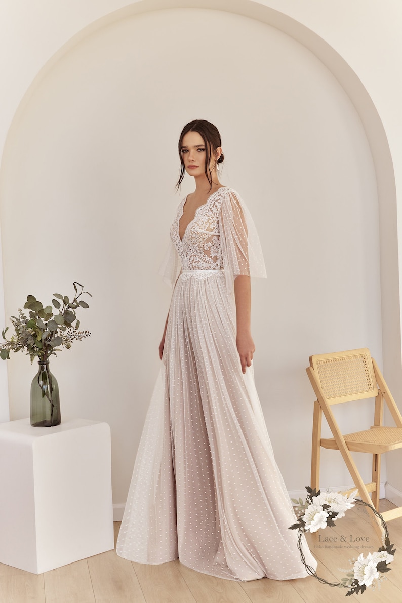 An ivory wedding dress with a lace bodice and a tulle skirt with polka dots. The dress has a V-neckline and short sleeves.