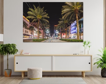 May include: A night view of a street in New Orleans, Louisiana, with palm trees lining the street and buildings lit up with colorful lights.