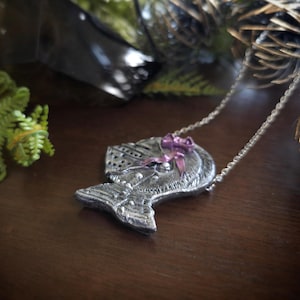 this image shows a hand sculpted knights helmet in silver color. the helmet is decorated with a pink bow