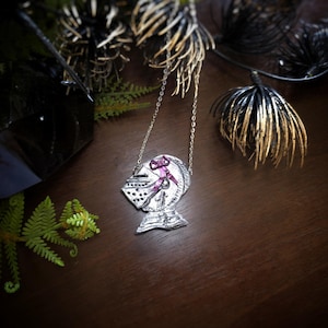 this image shows a hand sculpted knights helmet in silver color. the helmet is decorated with a pink bow