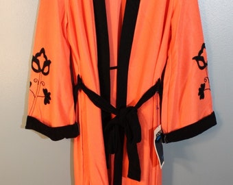 May include: An orange robe with black trim and a matching belt. The robe features black floral embroidery on the sleeves and black trim along the collar and cuffs. The robe is hanging on a wooden hanger.