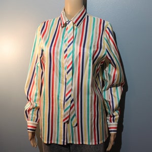 Könnte beinhalten: Ein langärmliges Hemd mit Knöpfen und einem bunten Streifenmuster in Rot-, Blau-, Grün-, Gelb- und Beigetönen. Das Hemd hat einen weißen Hintergrund und eine passende Krawatte.