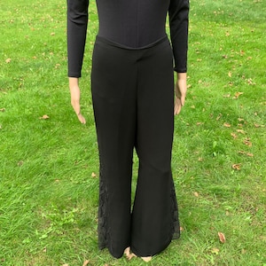 Puede incluir: Pantalón negro de pierna ancha con ribete de encaje a los lados. El pantalón está hecho de una tela suave y fluida.