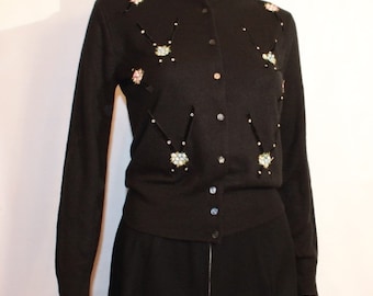May include: Black cardigan sweater with long sleeves and a button front. The sweater is embellished with rhinestones and other decorative elements in a geometric pattern.