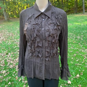 May include: A brown long-sleeved button-up shirt with a ruffled design on the front. The shirt has a collar and long sleeves with bell-shaped cuffs.