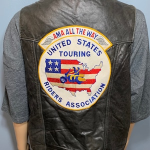 May include: Black leather motorcycle vest with a large embroidered patch on the back. The patch features a map of the United States with a motorcycle and the text "AMA All The Way United States Touring Riders Association".