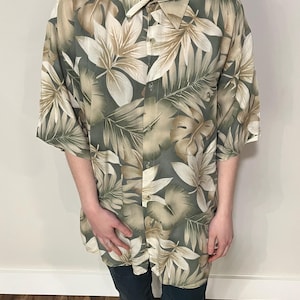 May include: A green and beige short-sleeved button-down shirt with a tropical leaf print.