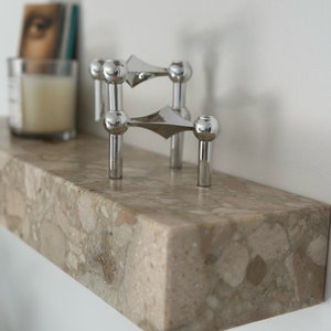 Può includere: Due portacandele argentati con un design geometrico si trovano su uno scaffale in marmo marrone chiaro.