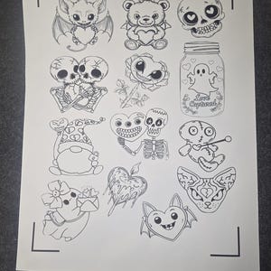 May include: A sheet of paper with various black and white illustrations. The illustrations include a bat with a heart, a teddy bear with a heart, a skull, skeletons, a rose, a jar with a ghost, a gnome, a voodoo doll, a pig, a heart with flames, and a cat.