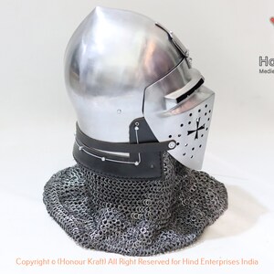 May include: A silver helmet with a visor and a chainmail coif. The helmet has a cross on the visor and is made of metal. The helmet is on a white background.