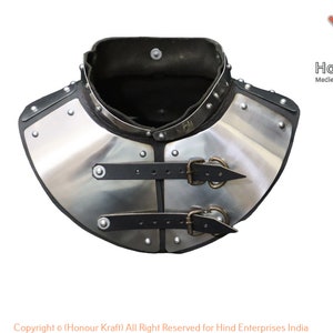 Könnte beinhalten: Ein silberner Nackenschutz aus Metall mit zwei schwarzen Lederriemen und Schnallen. Der Nackenschutz ist mit Nieten verziert und hat ein schwarzes Lederfutter.