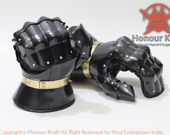 May include: A pair of black metal gauntlets with brass accents. The gauntlets are designed to protect the hand and fingers during combat. The gauntlets are made of steel and have a riveted construction. The gauntlets are worn on the left and right hands.