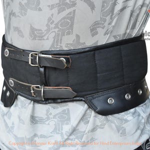 Könnte beinhalten: Schwarzer Leder- und gepolsterter mittelalterlicher Taillengürtel mit zwei Schnallenriemen und Nietendetails. Der Gürtel ist für Rüstungen konzipiert und trägt das Logo "Honour Kraft".