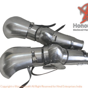 May include: A pair of silver metal knee armour with black leather straps. The armour is hand-forged and has a medieval design.