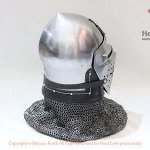 May include: A silver helmet with a face mask and a chainmail coif. The helmet has a pointed top and a leather strap around the bottom. The helmet is on a white background.