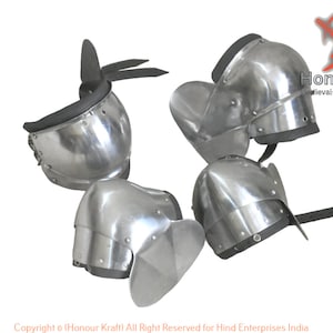 Puede incluir: Cinco rodilleras plateadas con correas de cuero negro. Las rodilleras son de metal y tienen una forma redondeada. Están diseñadas para proteger las rodillas de lesiones.