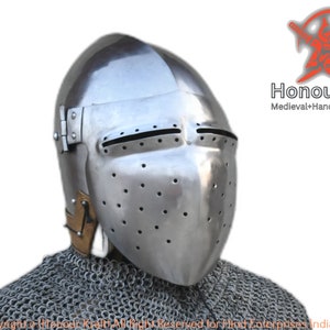 May include: A silver helmet with a visor and a chainmail collar. The helmet has a series of small holes throughout the visor and a hinged visor. The helmet is made by Honour Kraft, a company that specialises in hand-forged medieval armour.