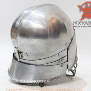 Op de afbeelding: Een zilveren helm met een vizier en een nekbeschermer. De helm heeft een getextureerd oppervlak en een decoratieve rand rond de onderkant. De helm is gemaakt van metaal en is ontworpen voor historische heropvoering of cosplay.