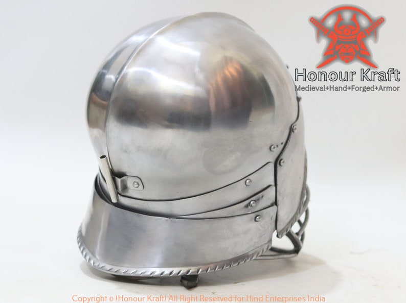 Op de afbeelding: Een zilveren helm met een vizier en een nekbeschermer. De helm heeft een getextureerd oppervlak en een decoratieve rand rond de onderkant. De helm is gemaakt van metaal en is ontworpen voor historische heropvoering of cosplay.