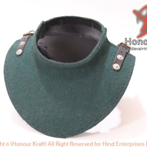 Könnte beinhalten: Ein dunkelgrünes mittelalterliches Gorget aus Filz mit schwarzem Innenfutter. Das Gorget hat Lederriemen mit Metallschnallen auf beiden Seiten. Es schützt Hals und oberen Brustbereich. Der Markenname "Honour Kraft" ist sichtbar.