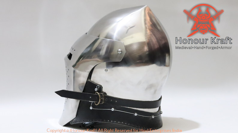 May include: A silver medieval helmet with a pointed top and a leather chin strap. The helmet is made of metal and has a textured surface. The helmet is a replica of a historical helmet.
