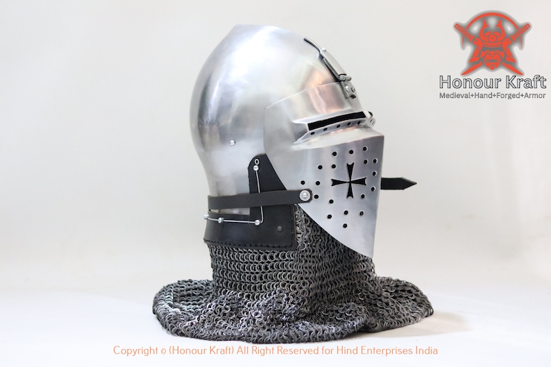May include: A silver helmet with a visor and a chainmail coif. The helmet has a cross on the visor and is decorated with small holes. The helmet is on a white background.