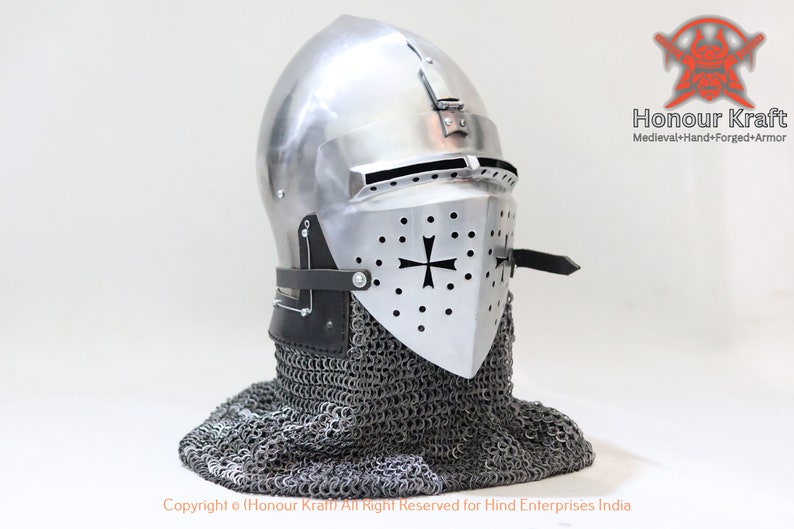 May include: A silver helmet with a black cross and a chainmail coif. The helmet has a visor and a pointed top. The helmet is made of metal and has a leather strap.