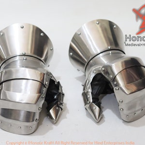 May include: A pair of silver medieval gauntlets with a pointed finger design. The gauntlets are made of metal and have a textured surface. The gauntlets are on a white background.