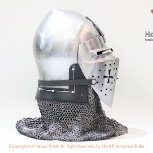 May include: A silver helmet with a faceplate and a chainmail coif. The helmet has a cross on the faceplate and is made of metal. The helmet is on a white background.