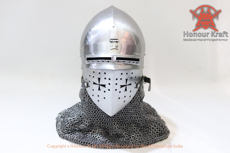 May include: A silver helmet with a visor and a chainmail coif. The helmet has a cross design on the visor and is decorated with small rivets. The helmet is on a white background.