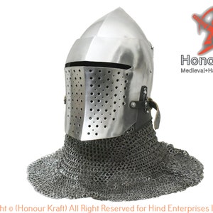 May include: A silver helmet with a face mask and chainmail coif. The helmet has a pointed top and a visor with small holes. The chainmail coif is made of interlocking metal rings. The helmet is a medieval style helmet.