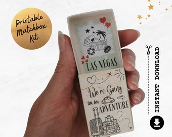 May include: A clear matchbox with a Las Vegas theme. The matchbox features illustrations of a slot machine, palm trees, and hearts. The text "We're Going on an Adventure" is also visible.