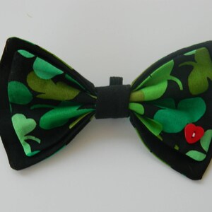 May include: A black bow tie with a green shamrock pattern and a red button in the center.