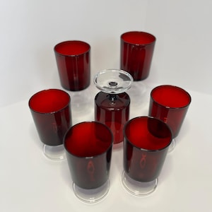 Könnte beinhalten: Satz von sieben roten Schnapsgläsern aus Glas mit klaren Glasböden. Die Gläser sind in einem Kreis angeordnet, wobei ein Glas in der Mitte steht.