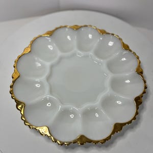 May include: White milk glass egg plate with a gold rim and scalloped edge. The plate has six individual sections for holding eggs.