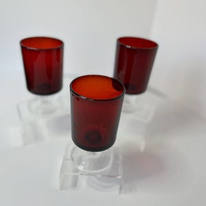 Peut inclure: Trois petits verres à shot en verre rouge transparent sur des supports en acrylique transparent.