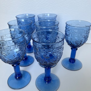 Könnte beinhalten: Satz von sechs blauen Glasbechern mit Stiel und einem strukturierten Traubendesign.