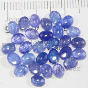Op de afbeelding: Een verzameling van 25 ovale, blauwe edelsteen cabochons. De stenen zijn glad en gepolijst, met een lichte glans.