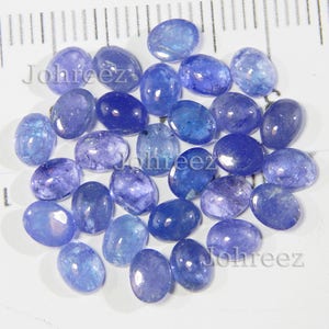 Op de afbeelding: Een verzameling van 25 ovale, blauwe edelsteen cabochons. De stenen zijn glad en gepolijst, met een lichtblauwe kleur en een lichte glans.